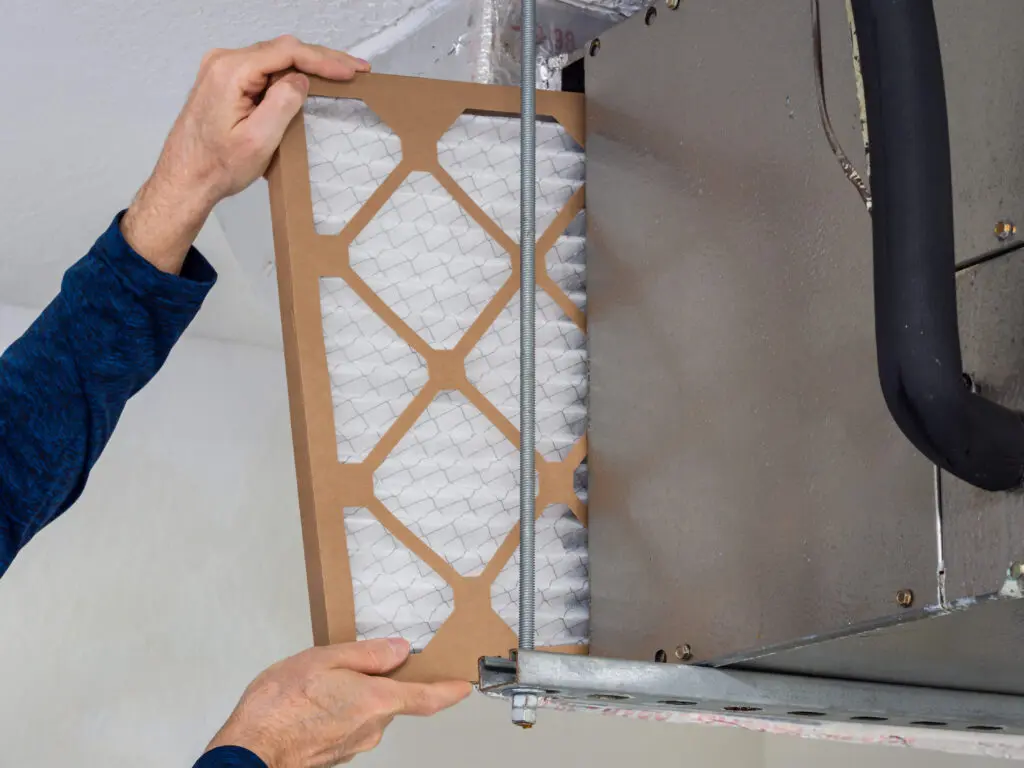 HVAC service technician changing dirty indoor air filter in residential heating and air conditioning system. Home air duct ventilation system maintenance for clean air.