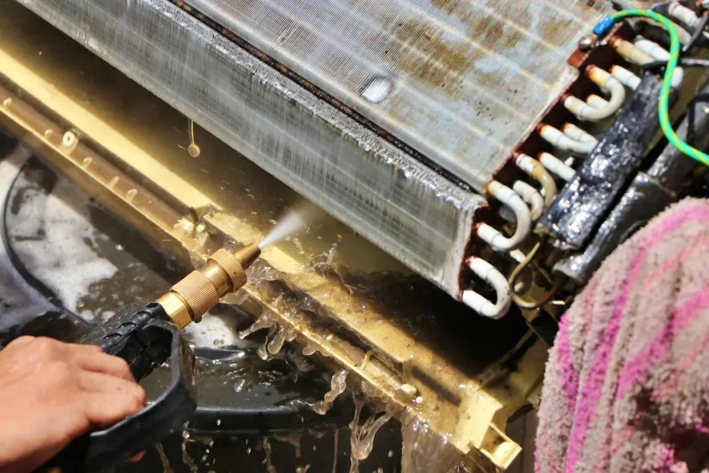 Wash away foam from air conditioner with high pressure water sprayer. Air conditioner maintenance, repair & service concept.