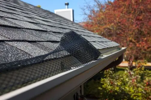 gutter guard installation services A close-up of a house roof shows a black mesh gutter guard being installed, with autumn trees in the background.