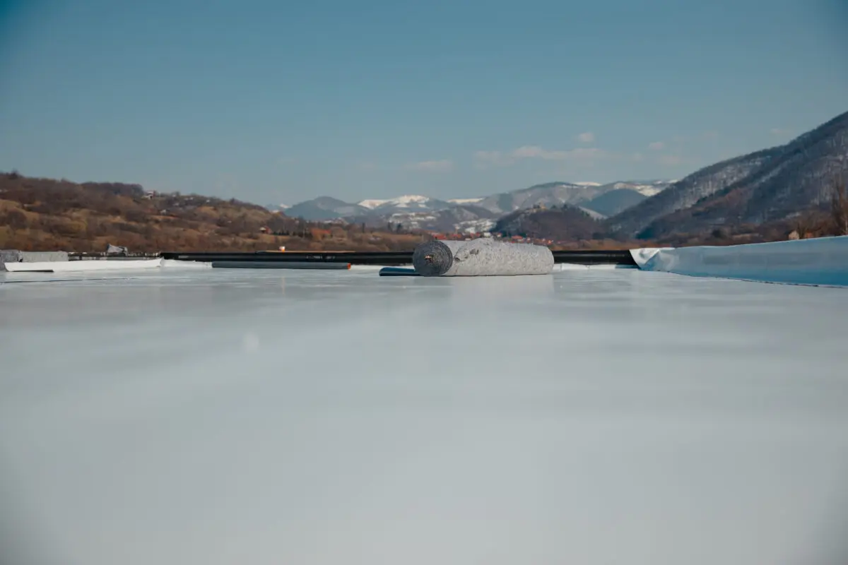 commercial flat roof repair A roll of roofing material lies on a flat, white roof with mountains and a clear blue sky in the background.