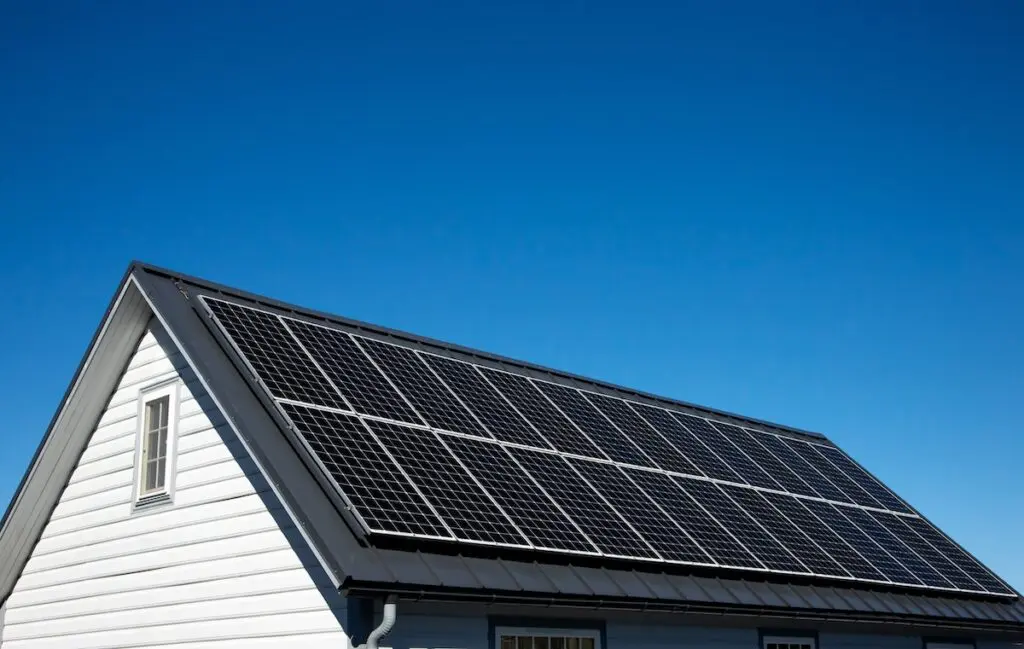 A white house with a steep roof in Madison is adorned with solar panels under a clear blue sky. The solar installation is neatly arranged, maximizing energy capture.