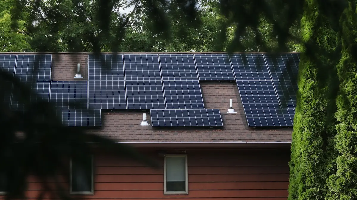 A house with brown siding in Stoughton features a sleek solar installation on its roof. The panels, meticulously arranged in rows around the roof vents, are framed by lush green trees, creating a harmonious blend with nature.