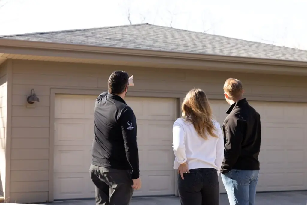 wisconsin solar incentives Three people stand outside in front of a garage with beige doors; one person is pointing toward the roof while the others look in the same direction. All are dressed in casual clothing.