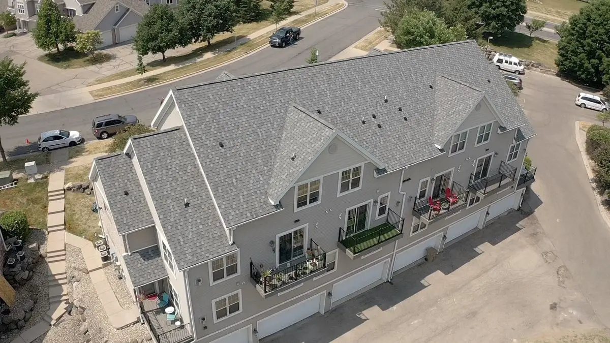 Aerial view of a modern, gray duplex townhouse with multiple balconies, garages underneath, and parked cars along surrounding streets in a suburban neighborhood.