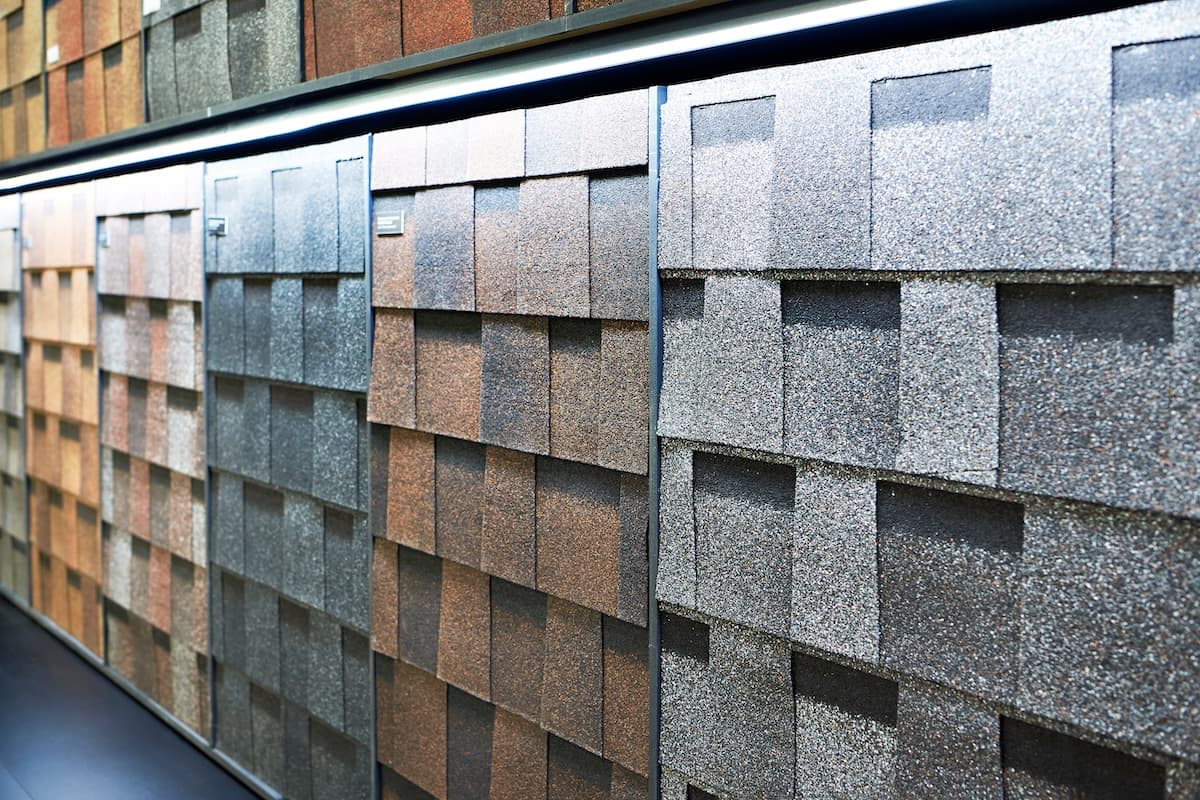 A display of the best roof shingles in various colors and textures, arranged in rows on a wall, showcases top options for roof materials in a showroom.