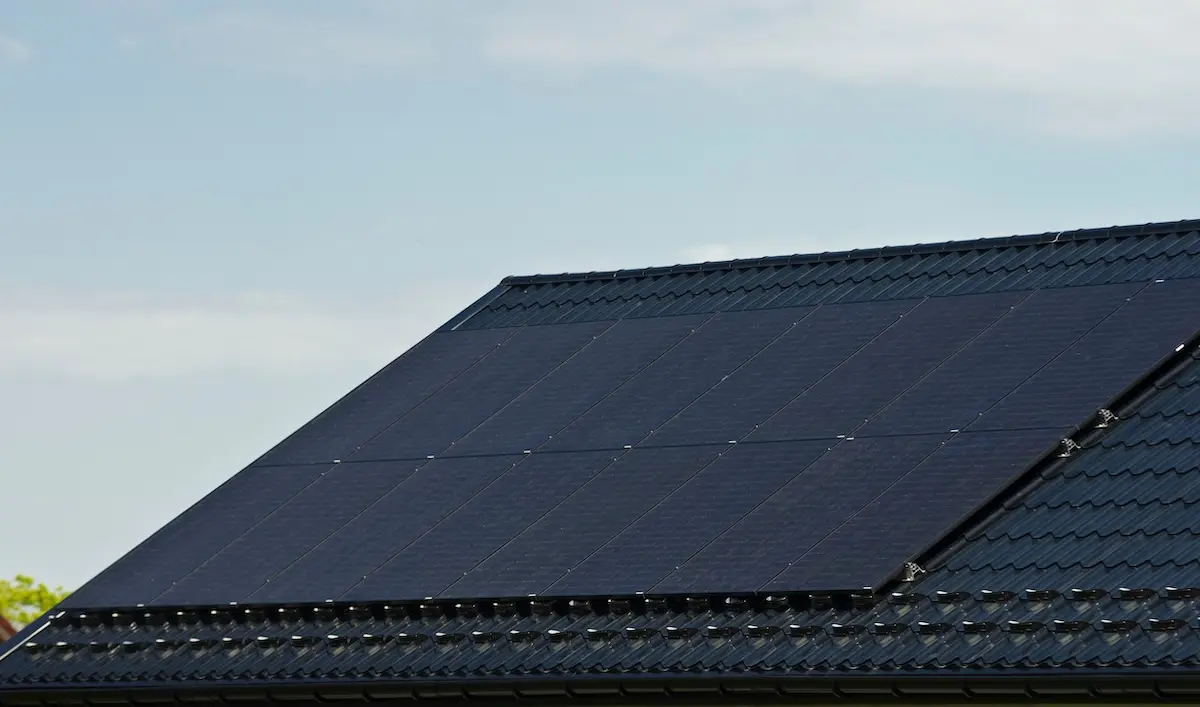 A rooftop in waunakee showcases a sleek solar installation, with several black panels elegantly arranged on the dark-tiled roof beneath a clear blue sky.