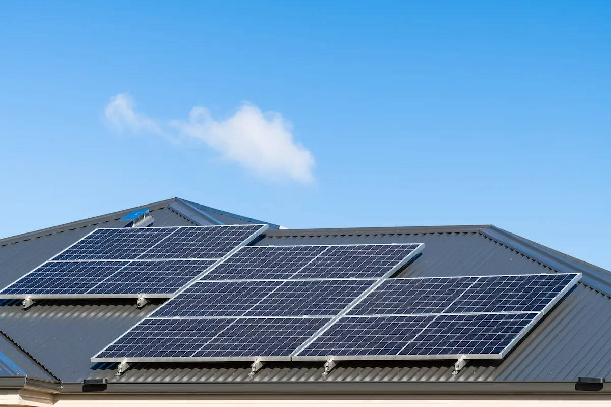 The rooftop in Madison showcases a solar installation with panels aligned perfectly under the clear blue sky. Resting on a corrugated metal roof, the setup shares space with a lone small cloud in the background.