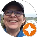 A person wearing glasses and a cap smiles at the camera. An orange star icon is overlaid at the bottom right corner of the image. The background shows a blurred outdoor scene.