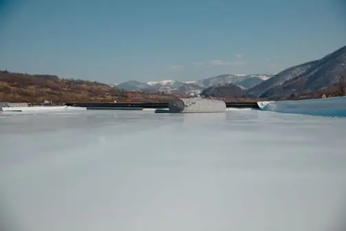 commercial flat roof repair A roll of roofing material lies on a flat, white roof with mountains and a clear blue sky in the background.