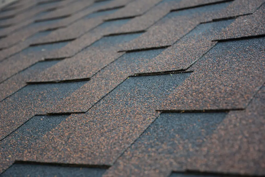 Close-up view of overlapping architectural shingles in shades of brown and black, arranged diagonally in a repeating pattern. architectural shingles