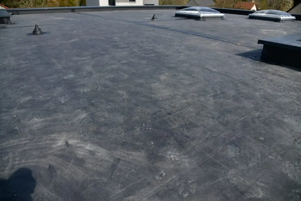 Flat rooftop covered with dark rubber roofing material, likely EPDM in comparison to TPO vs EPDM options, featuring several small rooftop vents and two roof windows or skylights. The surface appears slightly dusty and weathered under daylight.