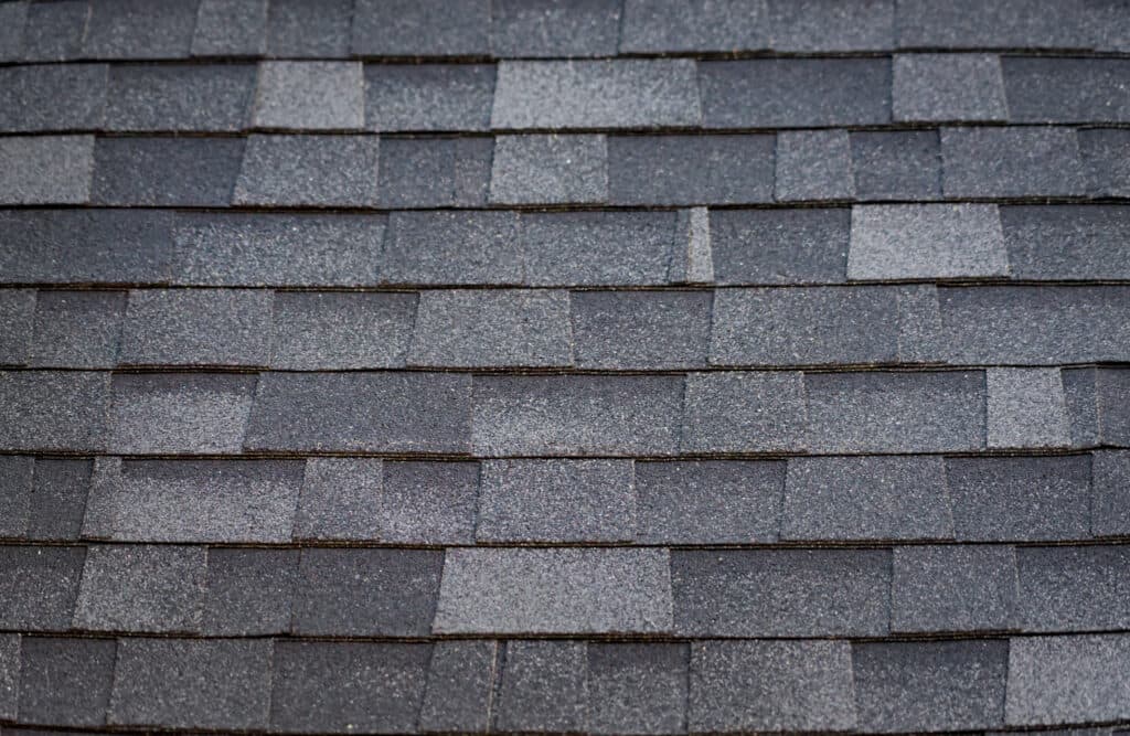 Close-up view of gray architectural shingles arranged in a uniform overlapping pattern, showcasing the textured and slightly varied surface of the roofing material.