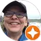 A person wearing glasses and a cap smiles at the camera. An orange star icon is overlaid at the bottom right corner of the image. The background shows a blurred outdoor scene.