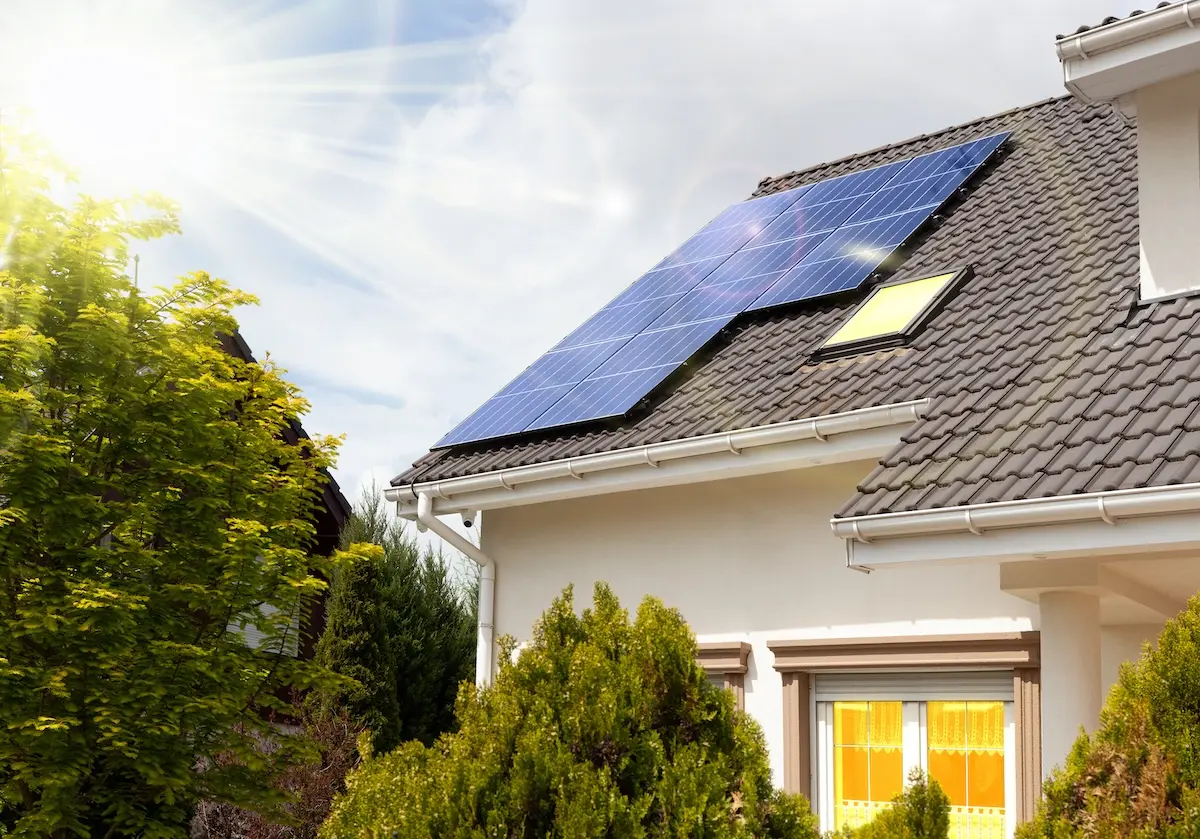 A sunny day highlights the solar installation in Middleton, with panels gleaming on the sloped roof of a house featuring cream walls and brown tiles. Green shrubs and trees surround the home, while sunlight beams down from the top left corner.