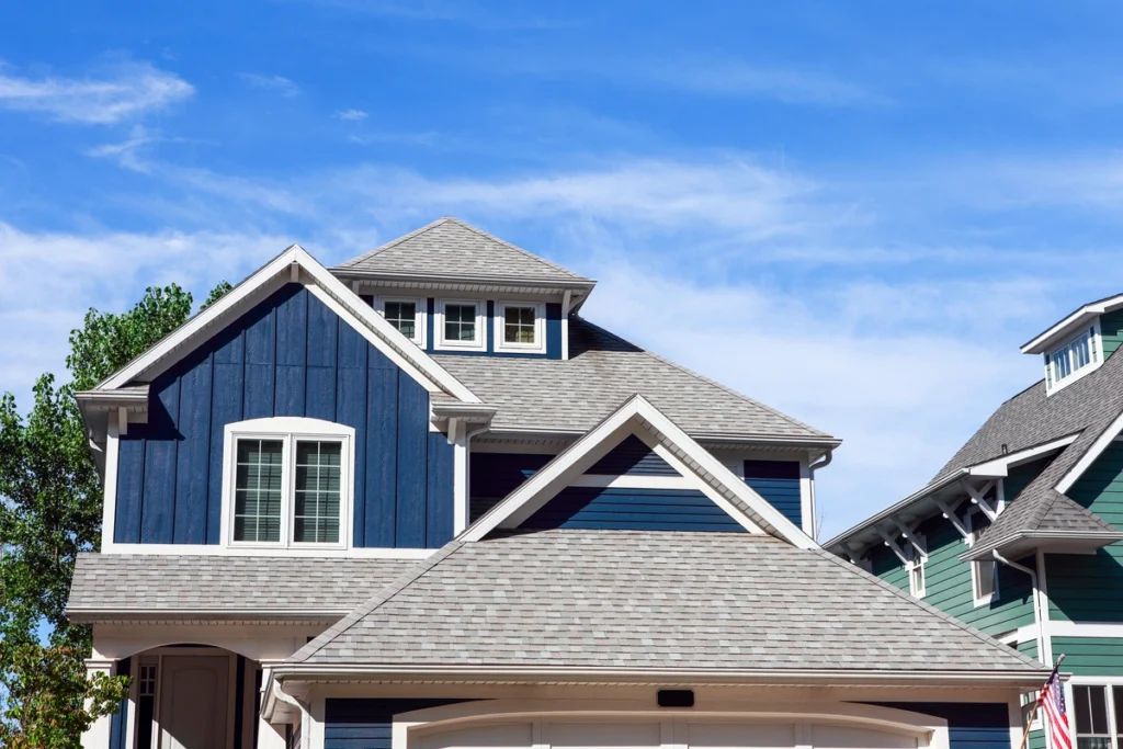 A blue two-story house with white trim and a gray roof showcases harmonious house and roof color combinations, featuring multiple peaked gables and several windows against a clear blue sky.