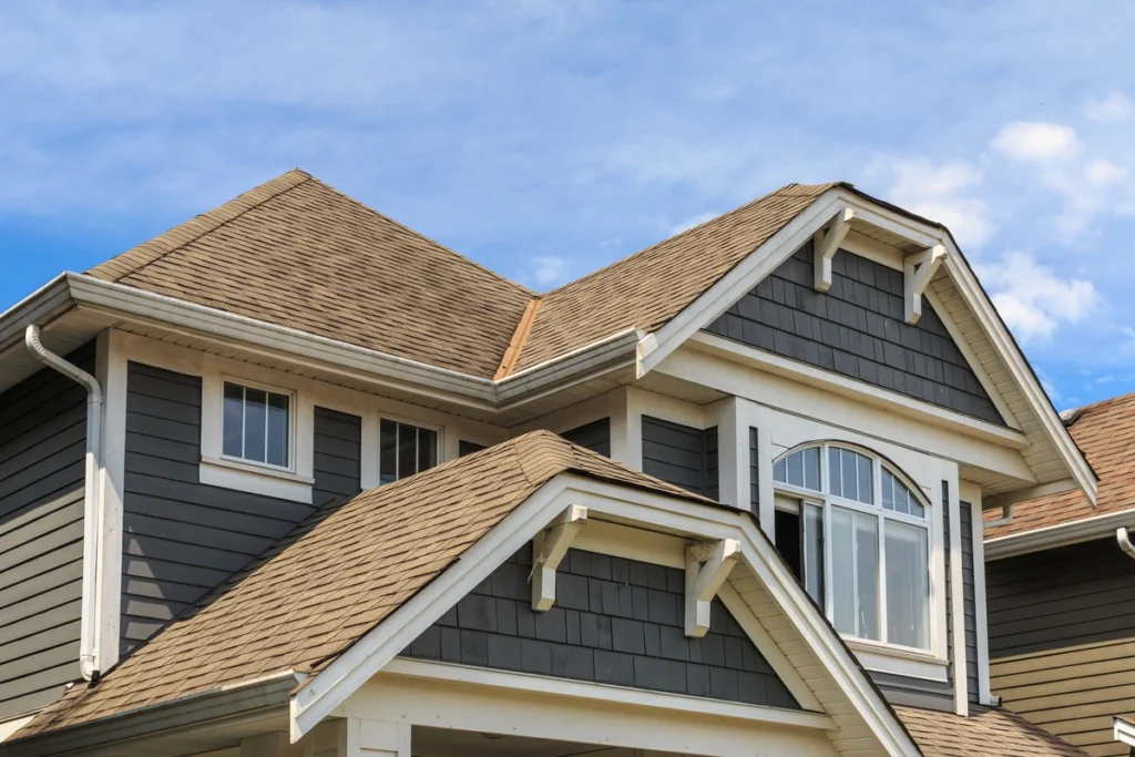 A modern suburban house showcases eye-catching house and roof color combinations with its gray siding and white trim under a clear blue sky. The roof highlights brown shingles set on dual gables, accentuated by a large arched window on the upper floor.