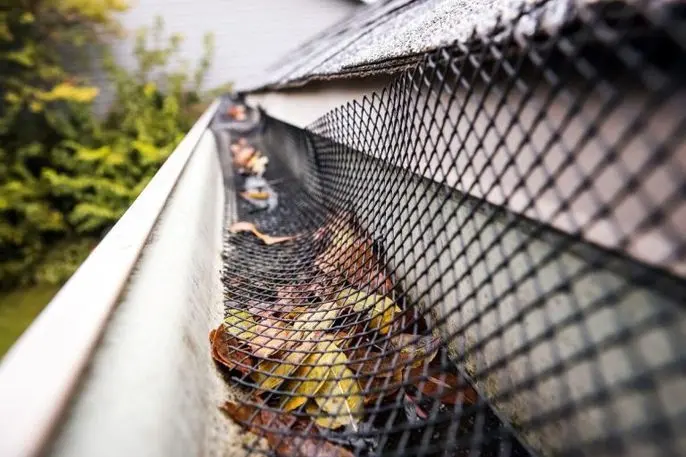 A black mesh gutter guard installed over a rain gutter filled with fallen leaves.