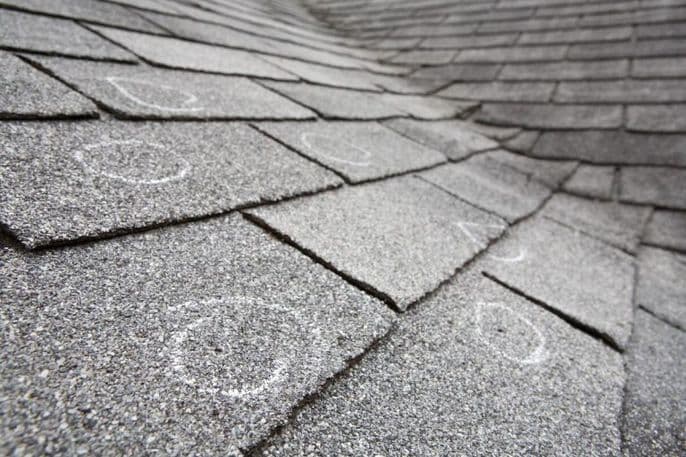 Asphalt roof shingles marked with white chalk circles to indicate damage requiring emergency roof repair.