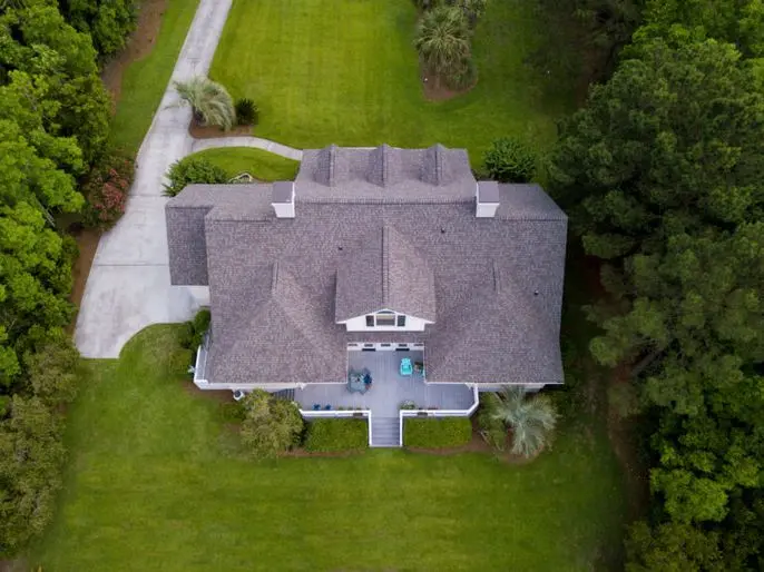 roof types Aerial view of a large house with a gray roof, surrounded by green grass, trees, and shrubs; a driveway curves to the left side of the property.