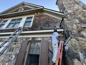 Painter applying paint to the stone wall of a large, beautiful house.