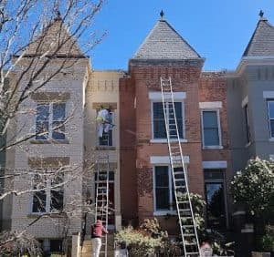 Restoration of a historic brick row house with workers painting the exterior.
