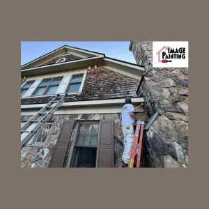 Professional house painting on exterior stone wall with ladders and painter.