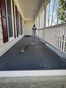 Professional porch painting on a spacious outdoor porch with a worker applying paint.