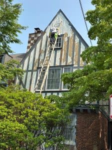 Tudor-style house renovation with worker painting exterior walls.