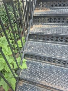 Metal staircase with decorative cutouts and surrounding green foliage.