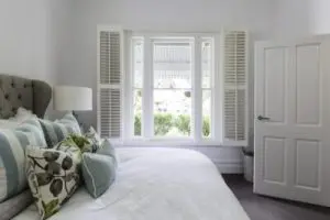 Bright bedroom featuring a large window with white shutters and a neatly made bed.
