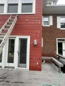 Red wooden house exterior with ladder and ongoing paint restoration.
