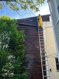 Professional house painting with a person on a ladder applying dark brown paint to the exterior wall.