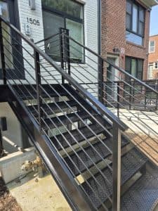 Exterior staircase with black metal railing and steps, leading to the entrance of a contemporary urb.
