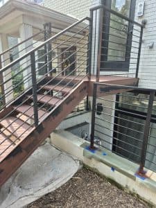 Outdoor metal staircase with black railing and wooden steps for residential access.