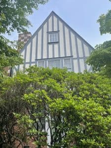 Tudor style house with black and white exterior and lush green bushes in front.
