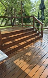 Wooden deck with stairs and railing in a lush outdoor setting.