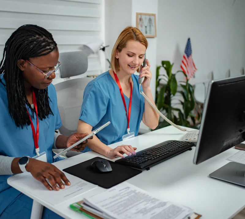 Two urgent care front desk employees, one answering a patient phone call