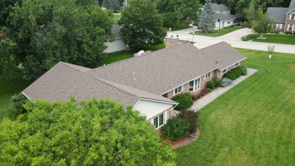 A house with a green lawn and a tree next to it. Asphalt shingle roof