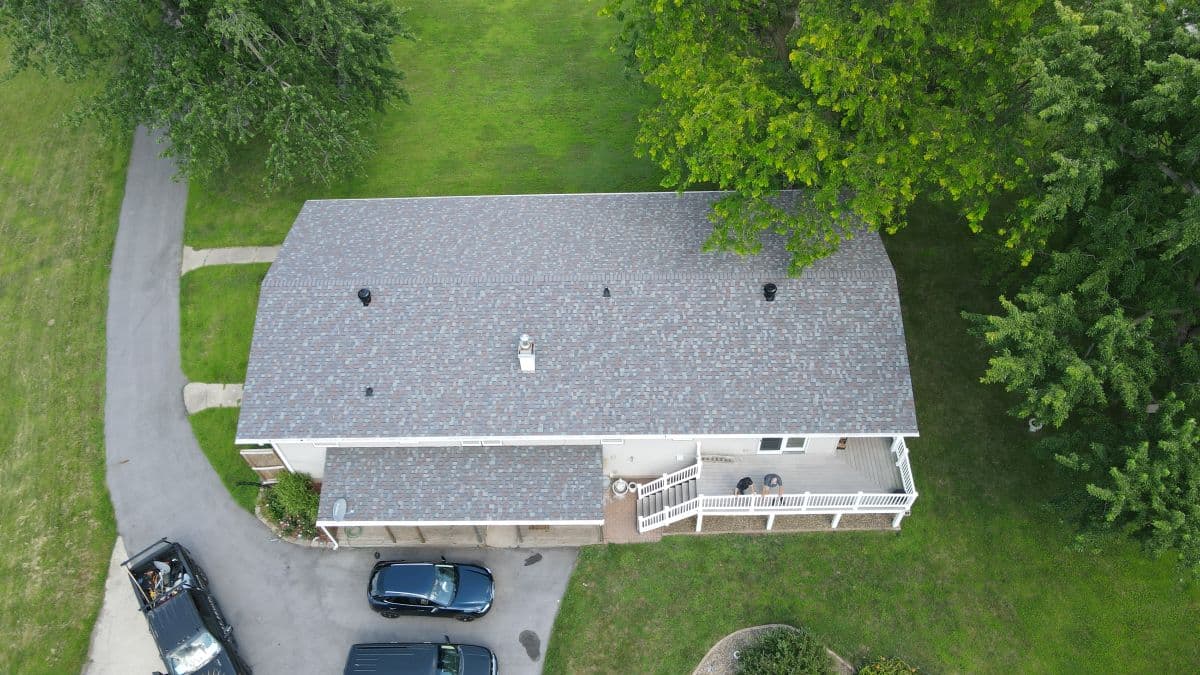 Aerial view of a light grey shingle roof on a house surrounded by greenery