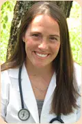 Professional portrait of Dr. Colby Burns smiling outdoors while wearing a white lab coat with a stethoscope around her neck.