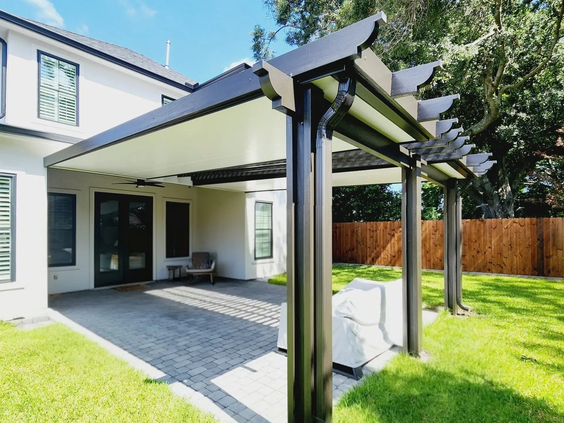 Custom aluminum patio cover with pergola centerpiece, featuring black and white design, shaded outdoor space in Metairie, Louisiana, ideal for comfortable living and natural ventilation.
