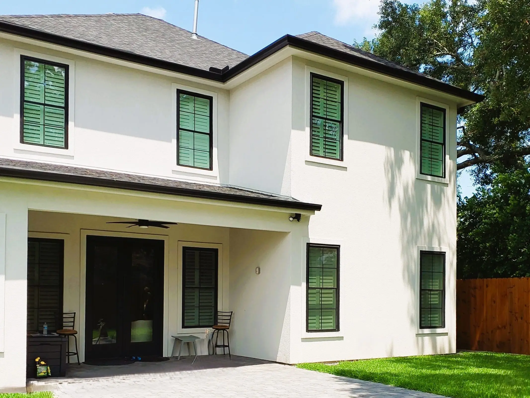 Modern home exterior in Metairie, Louisiana, featuring a stylish patio cover with a pergola, green shutters, and well-maintained lawn, emphasizing outdoor living and comfort.