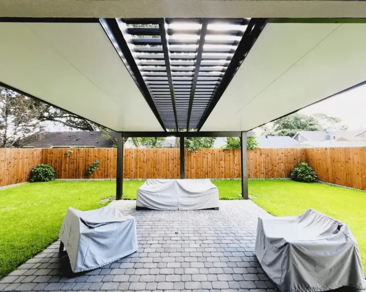 Patio cover with insulated laminated roof panels, providing shade and protection, featuring covered furniture and green lawn in a residential outdoor setting.