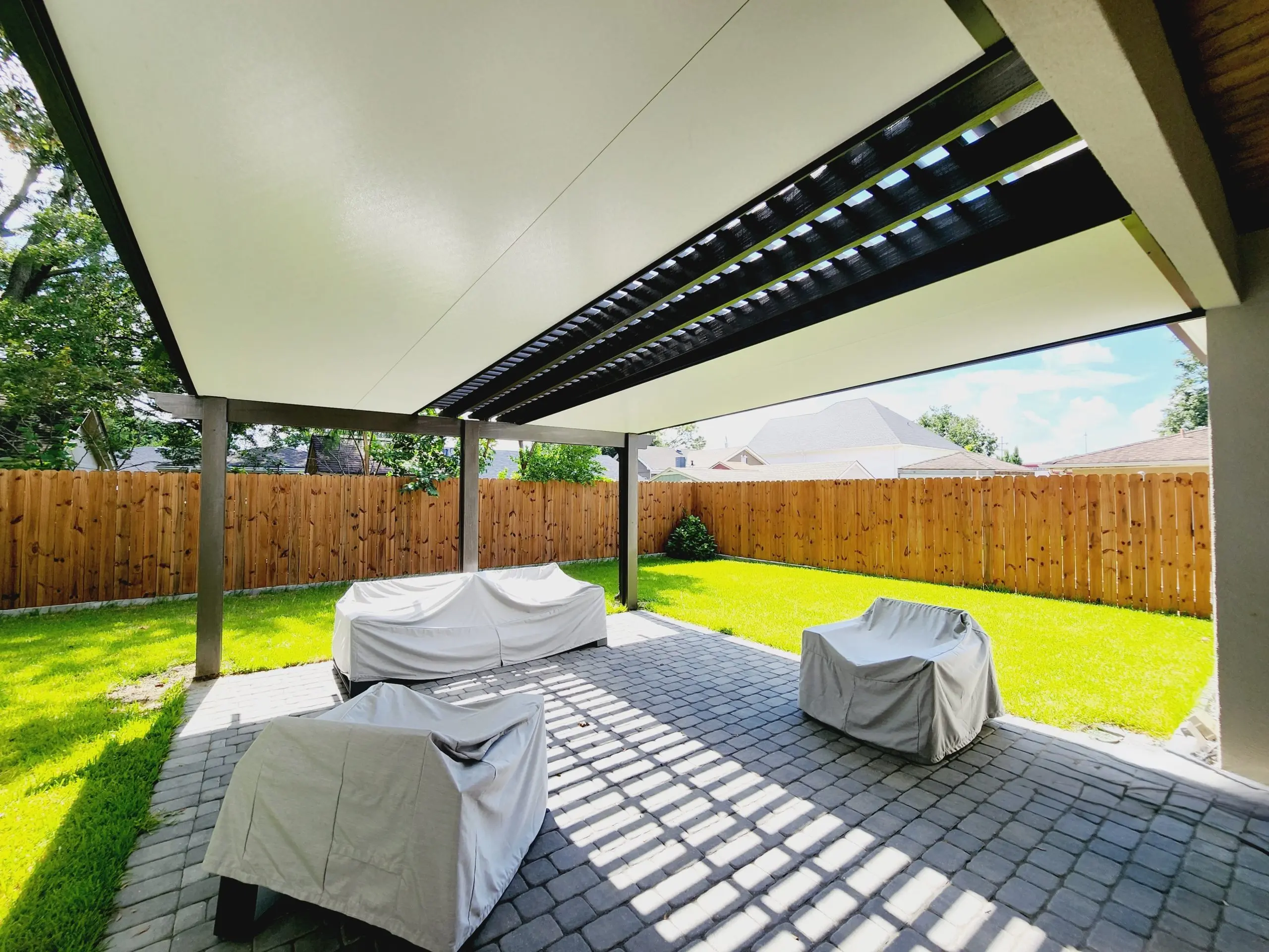 Luxurious outdoor patio cover with a 4-inch insulated aluminum roof, featuring a pergola centerpiece, shaded seating area, and landscaped yard in Metairie, Louisiana.