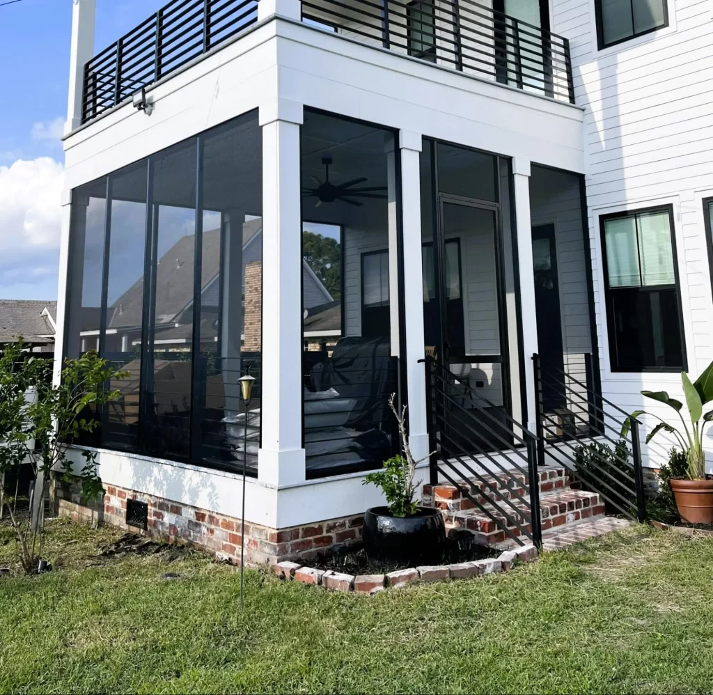 Screened-in porch with modern design, featuring large glass panels, black railings, and outdoor seating, enhancing outdoor living for Louisiana homes.