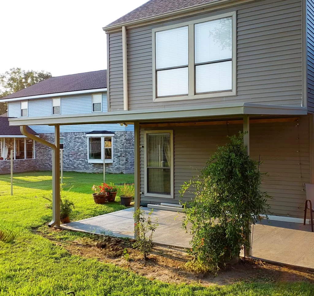 Patio cover featuring insulated roof panels attached to a home, surrounded by a green lawn and flower pots, showcasing a durable outdoor living space.