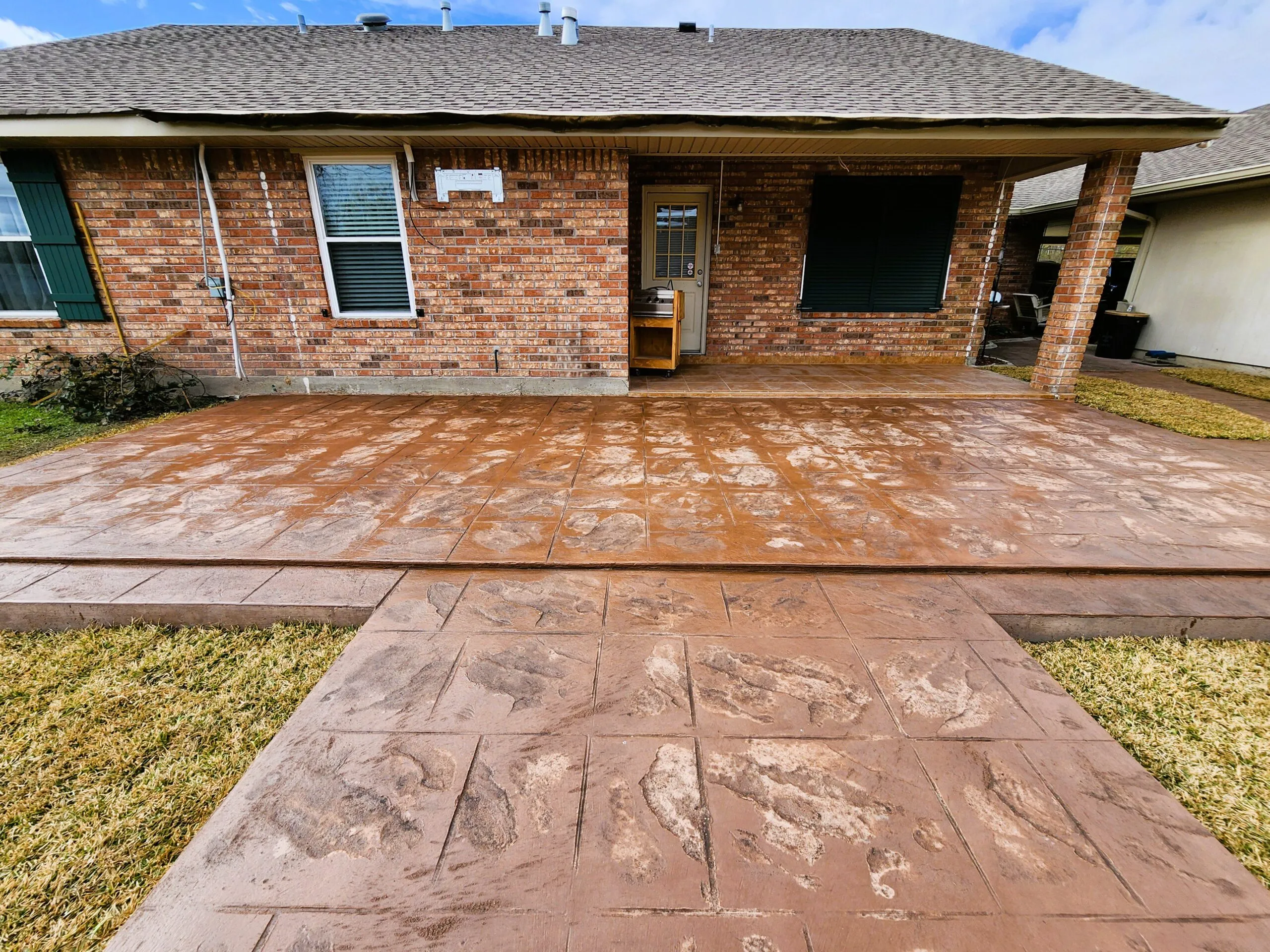 Concrete patio and walkway with stamped finish, adjacent to brick home, showcasing outdoor space for residential projects.