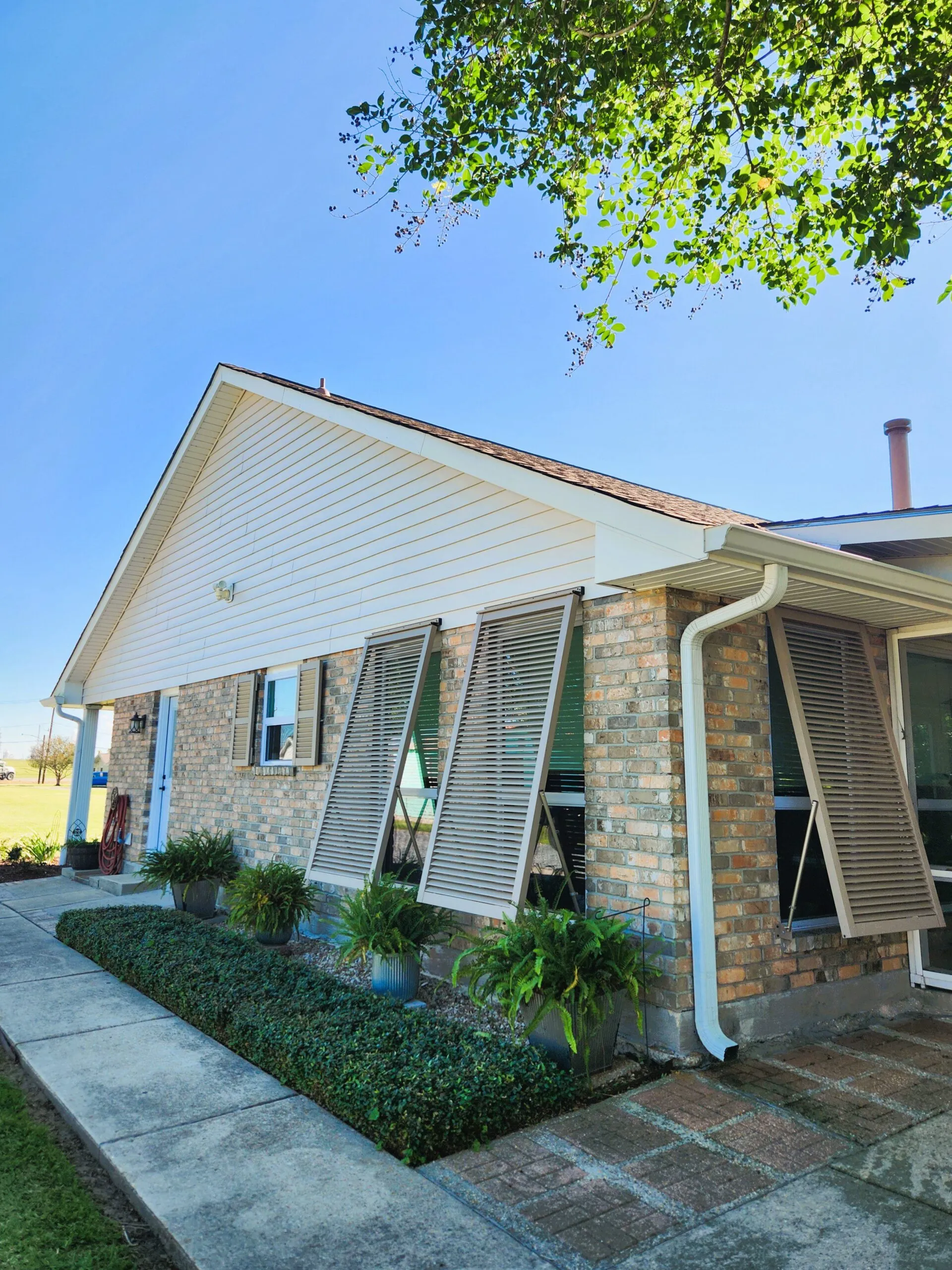 Exterior view of a home showcasing new vinyl siding installation, aluminum soffits, and custom fascia, surrounded by neatly trimmed landscaping and potted plants, emphasizing durability and aesthetic appeal.