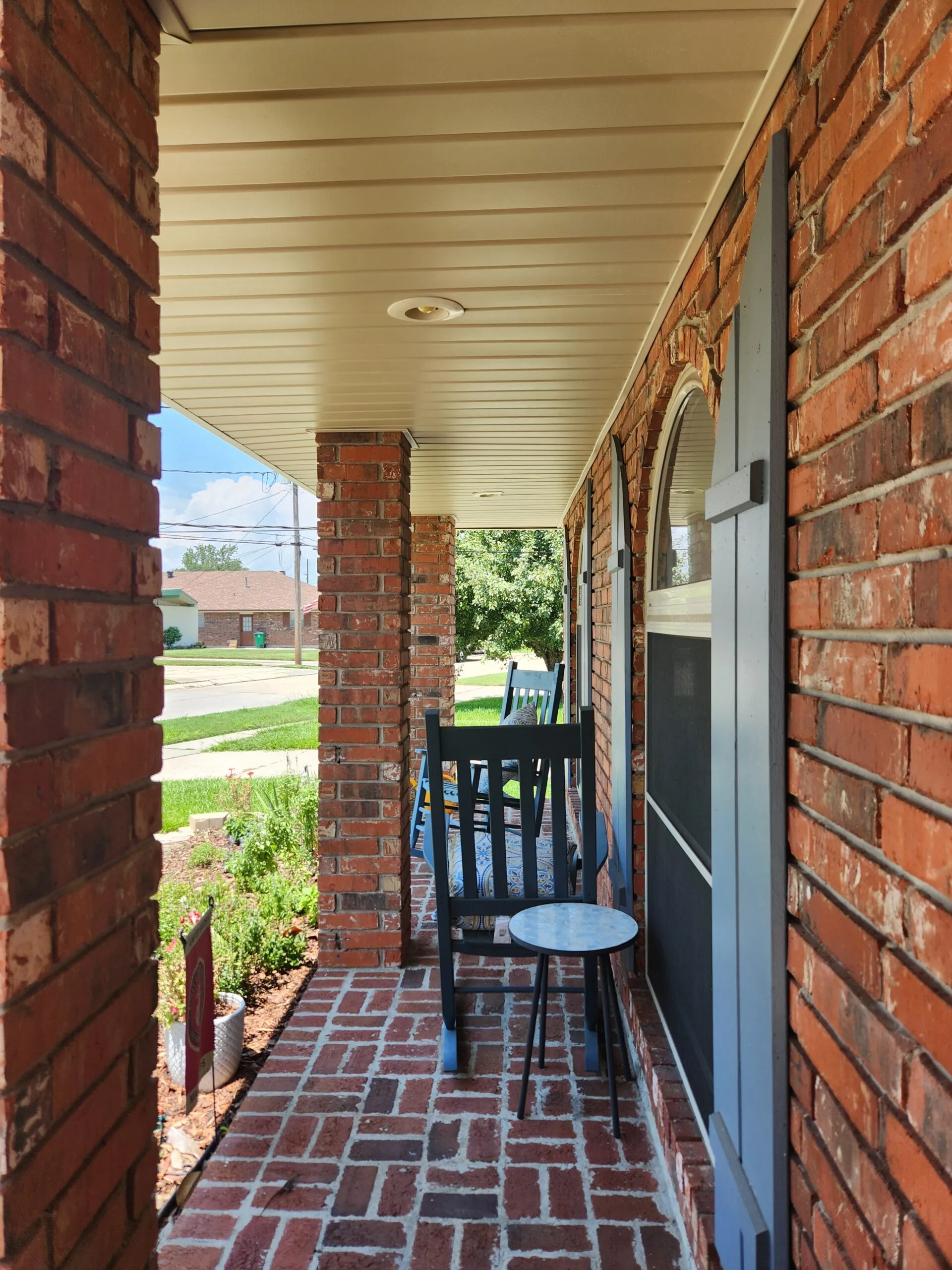 Porch view showcasing newly installed aluminum soffit and custom fascia, with a brick exterior, rocking chairs, and a small table, enhancing curb appeal and ventilation.