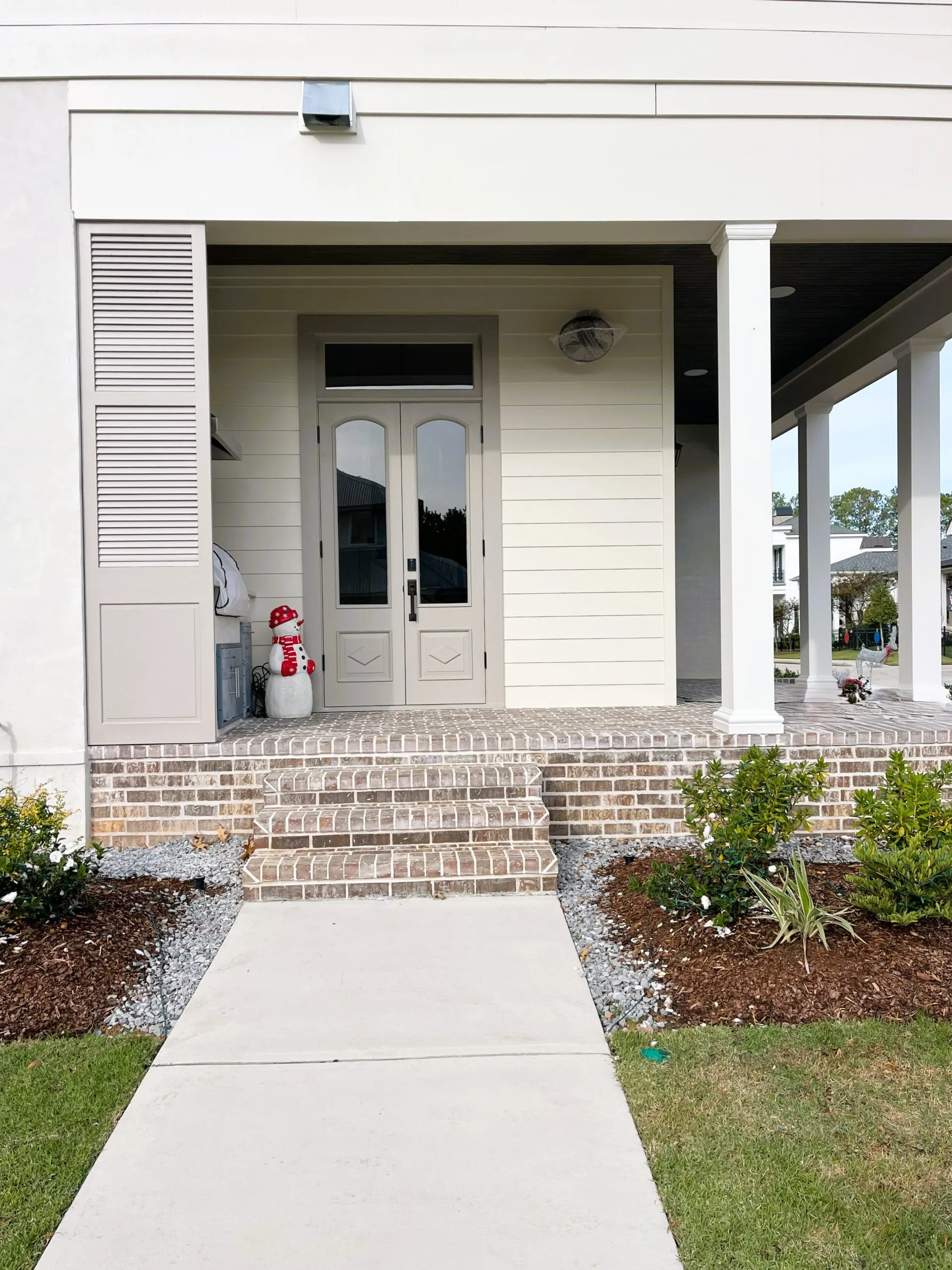 Front entrance of a home showcasing new vinyl siding, brick steps, and landscaped garden; features double doors and decorative soffit, emphasizing quality exterior installation services by Capital Improvement.